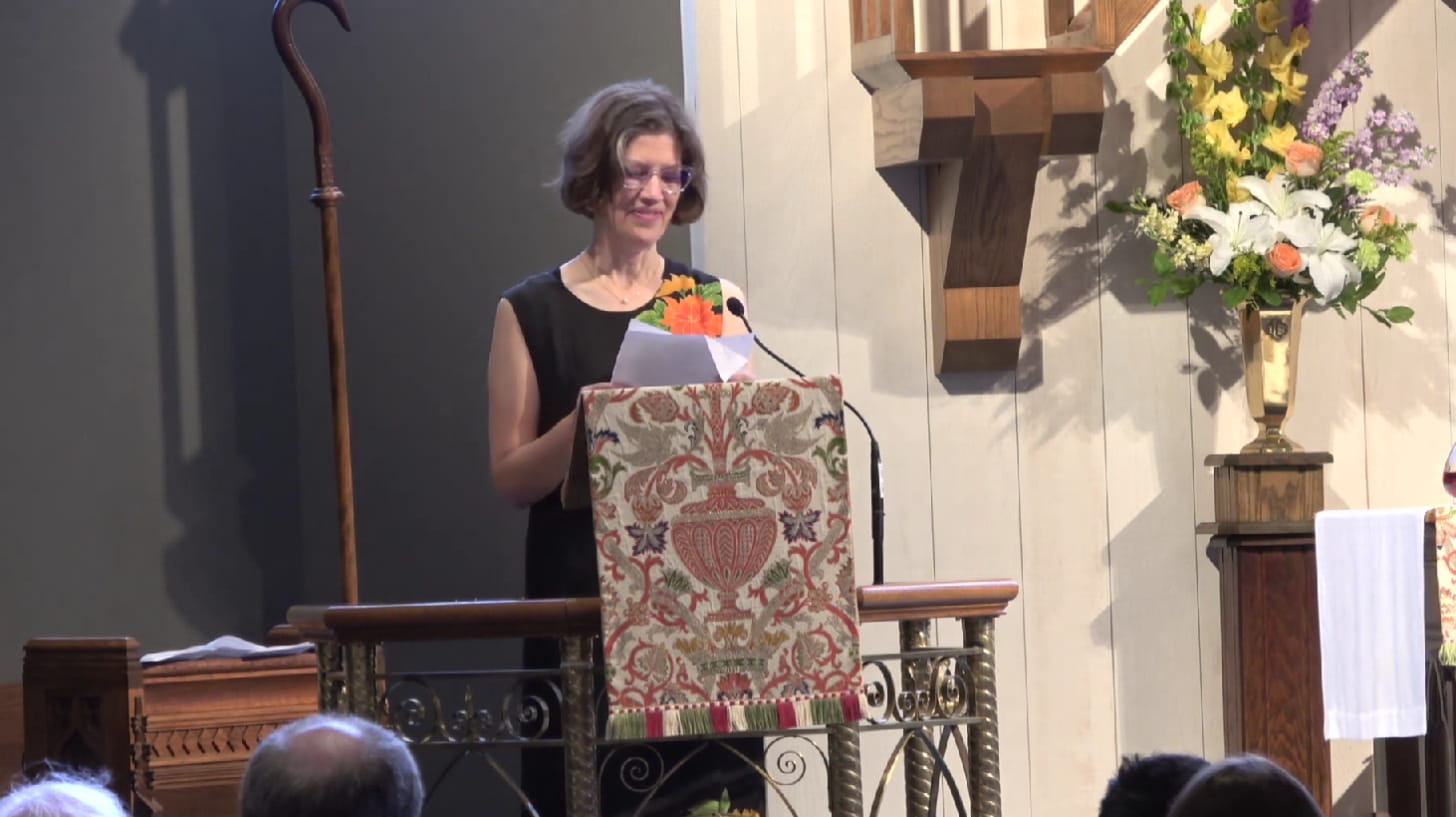 A middle-aged woman in black dress stands near flowers at the front of a church