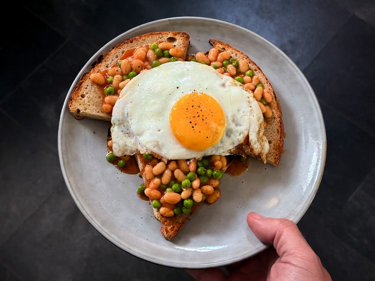 A fried egg sits on some peas and beans on sourdough toast