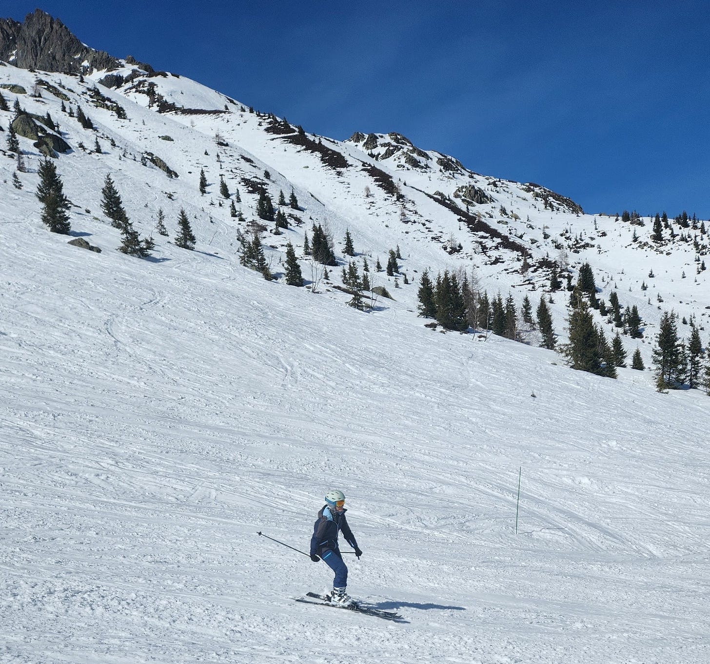 Montanha coberta de neve com uma pista de esqui com mulher toda vestida de azul desce esquiando.