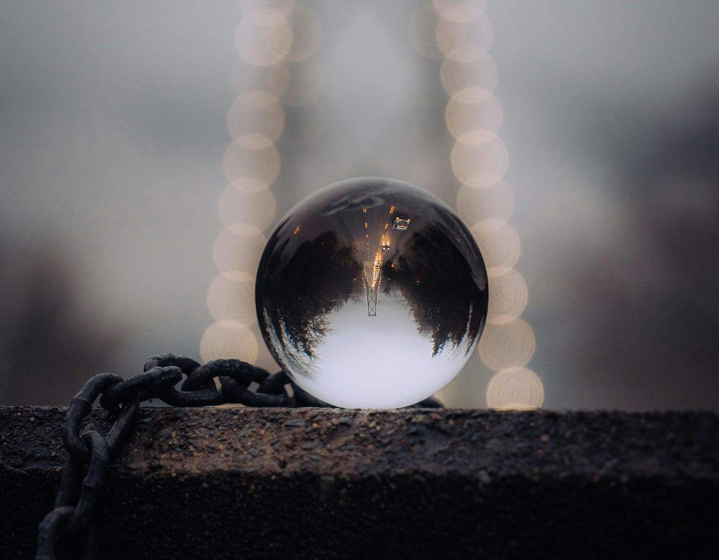 Glass lens ball with an inverted image of a bridge. Thick black chain underneath