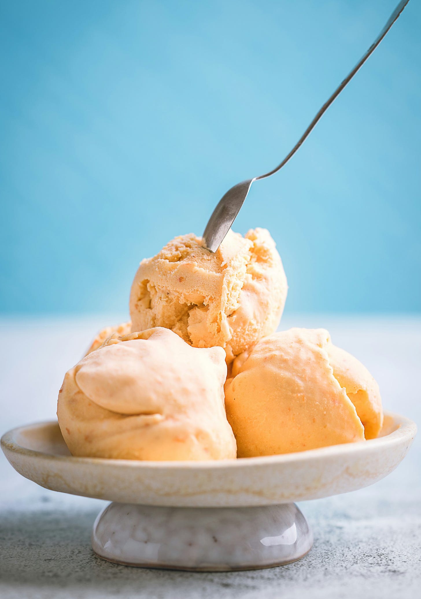 a picture of three scoops of vanilla ice cream with a spoon on top. The background is blue. 