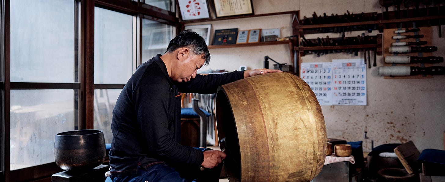 A photograph of Japanese traditional bell-maker, Yoshinori Shimatani, tuning a large temple bell.