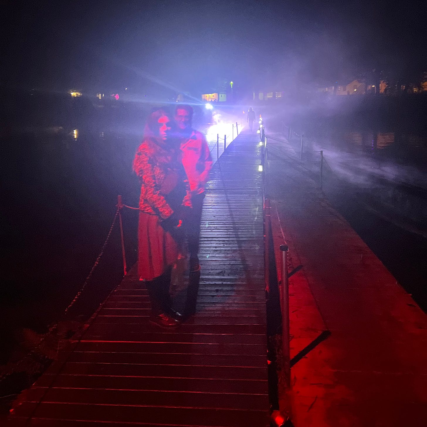 Two people posing on a skinny bridge over water at night