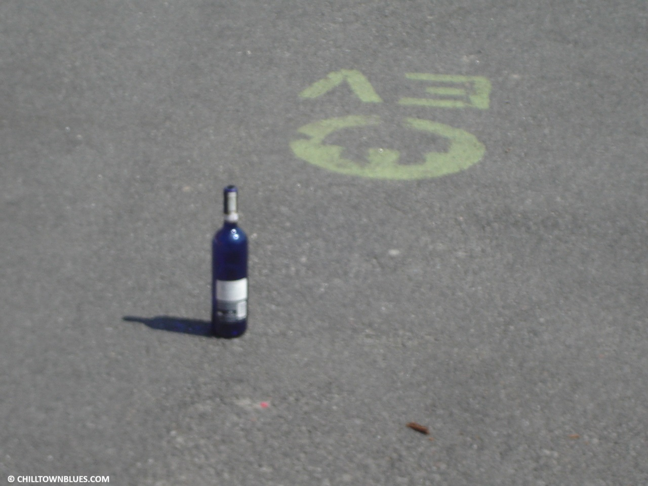 In a parking spot where an electric car can get recharged, someone has left a blue bottle of liquor. A cigar stub is about a foot away from it.