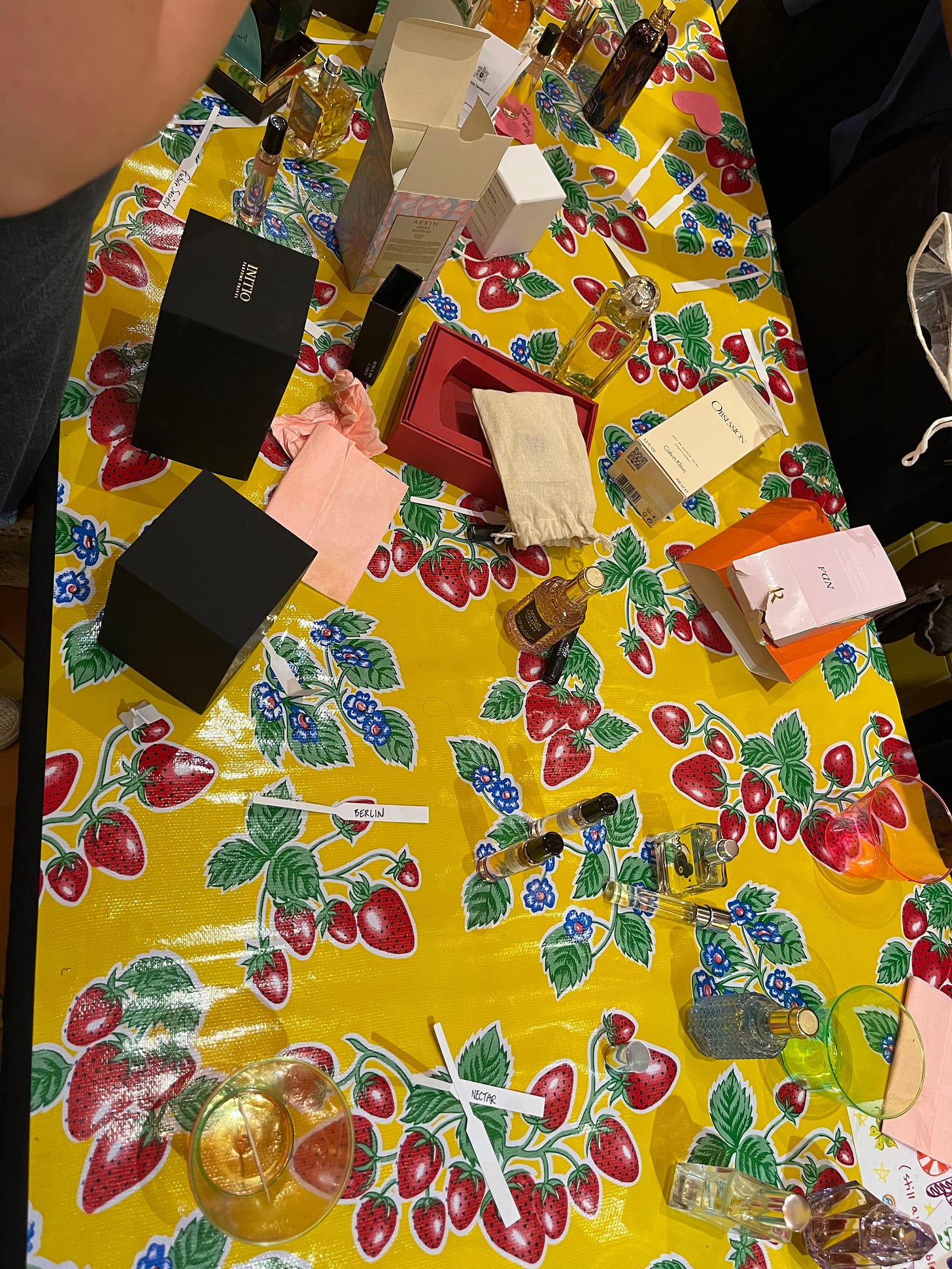 a messy table with a few boxes, fragrance blotters, and bottles of perfume on it