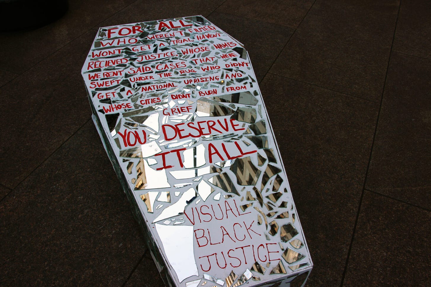 a white coffin lined with shattered mirrors and red handwriting reads: "“For all who weren’t filmed won’t get a trial haven’t received justice whose names weren’t said cases that were swept under the rug who didn’t get a national uprising and whose cities didn’t burn from grief you deserve it all VISUAL BLACK JUSTICE"