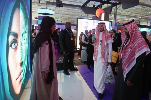 Two people interact with a robot placed in front of a digital screen, in a crowded room.