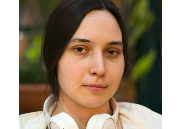 Photo of Harvard cancer researcher Kseniia Petrov, looking with a neutral expression at the camera, a set of white headphones around her neck