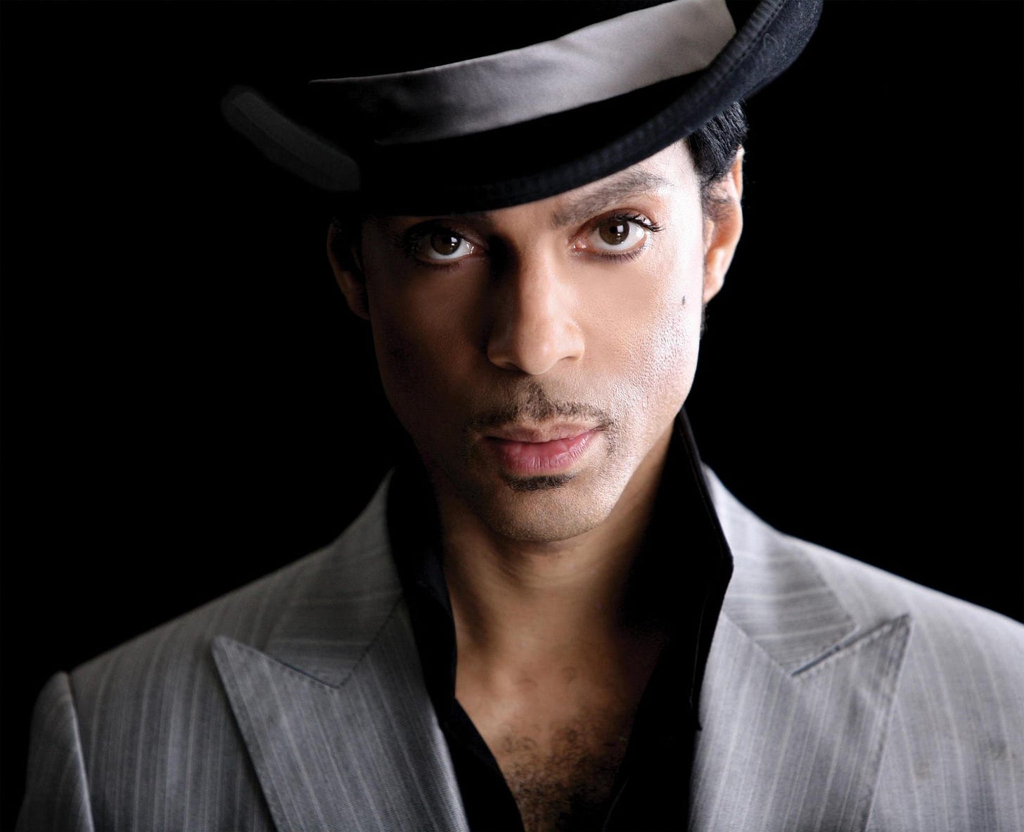 prince, grey suit, black shirt, hat with grey brim, black background. rocking a thin mustache and chest hair. he was a black man 

"i don't really care so much what people say about me because it usually is a reflection of who they are. for example, if people wish i would sound like i used to sound, then it says more about them than it does me."