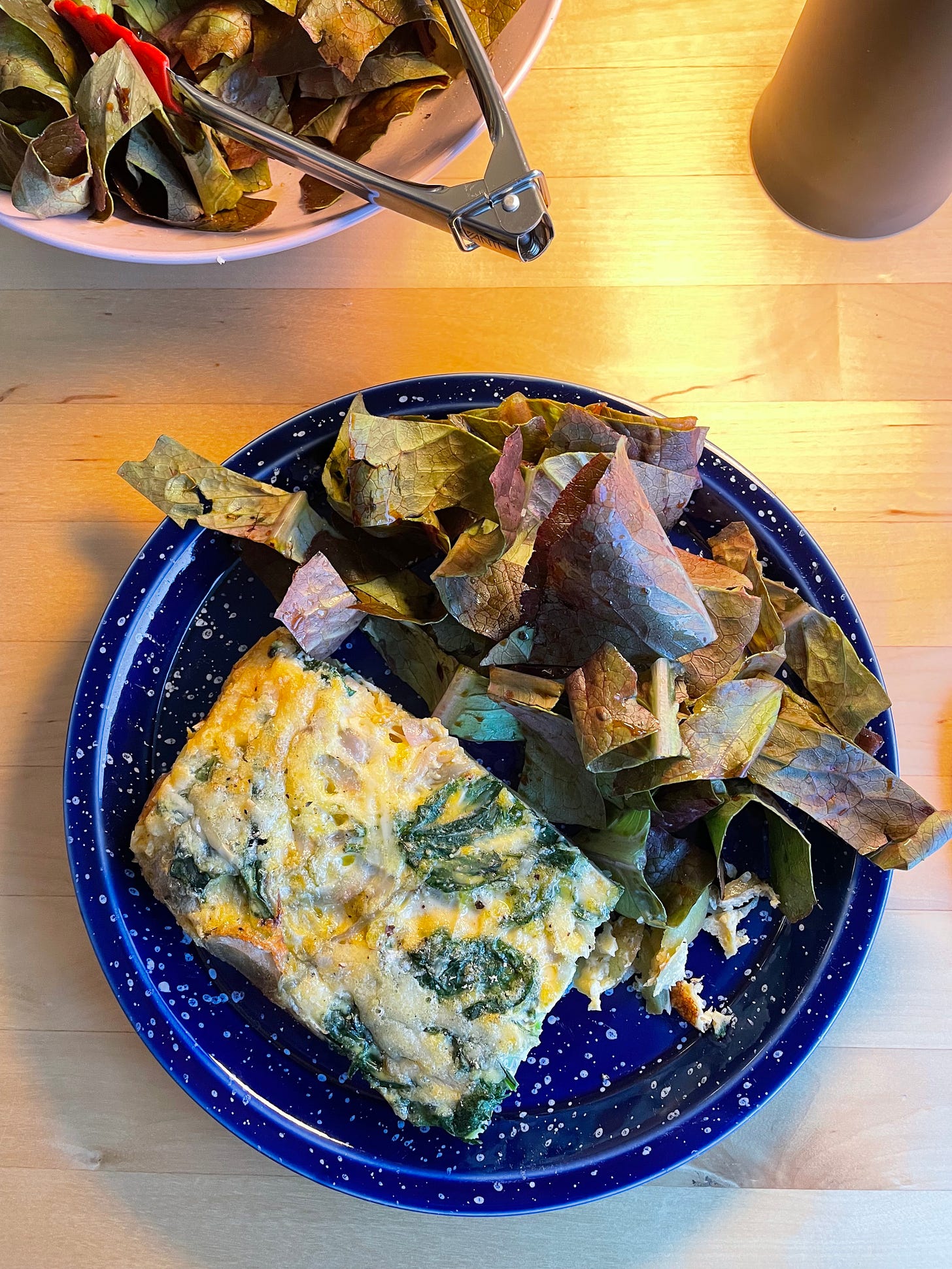 Slab of frittata made with spinach and cheese on a blue speckled plate, a dark leaf salad alongside it.