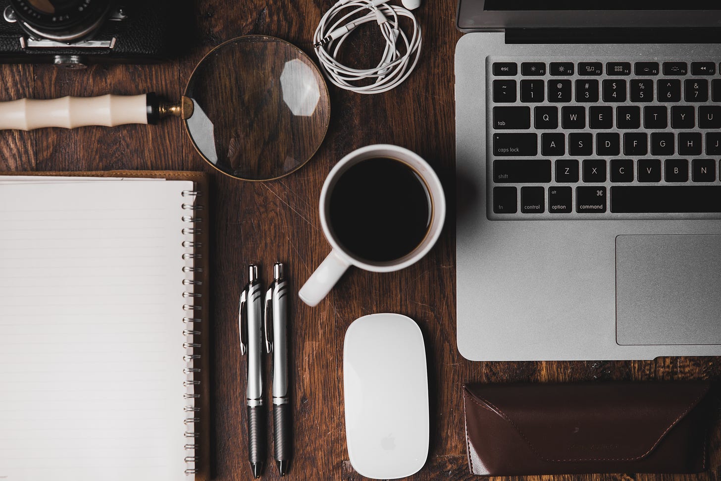 Desktop covered with coffee, computer, mouse, pens, magnifying glass, and other tools by Ian Dooley via Unsplash.