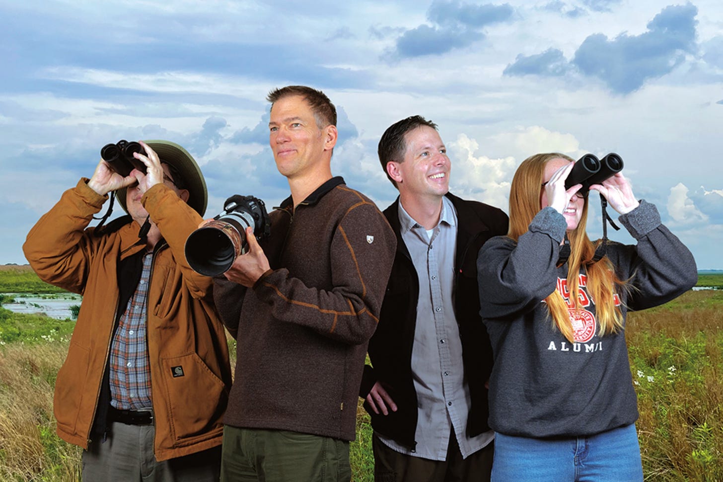 This photo is from an article in the Redbird Impact magazine about the Fluddles initiative. In the photo are biologist Angelo Capparella looking through binoculars, author Bill Davison with a camera, ISU Professor R.J. Rowley looking off into the distance, and ISU student Brittany Menzel looking through binoculars. The background is a wetland on a sunny day.