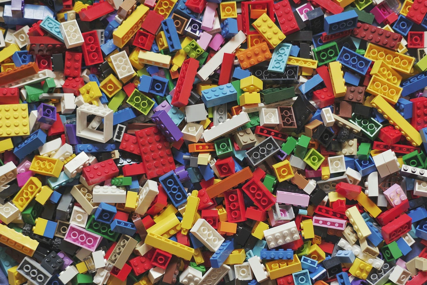Inquadratura aerea di tantissimi pezzetti diversi e colorati di mattoncini Lego sparsi.