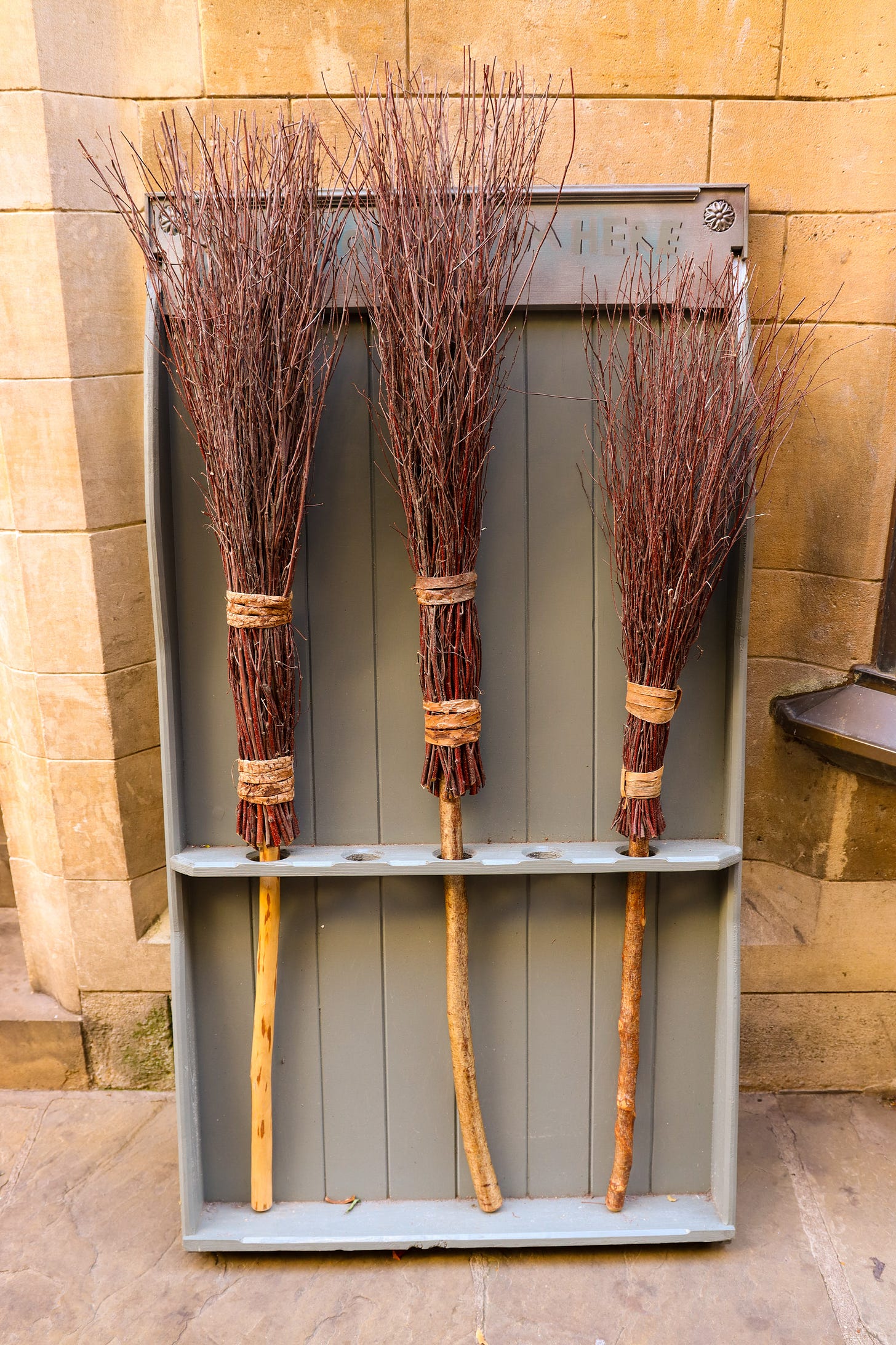 3 twig brooms in a broom stand outside a building 