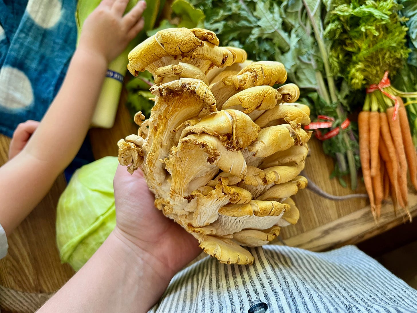 I'm holding a beautiful golden oyster mushroom, in the background my daughter grabs a bunch of leeks