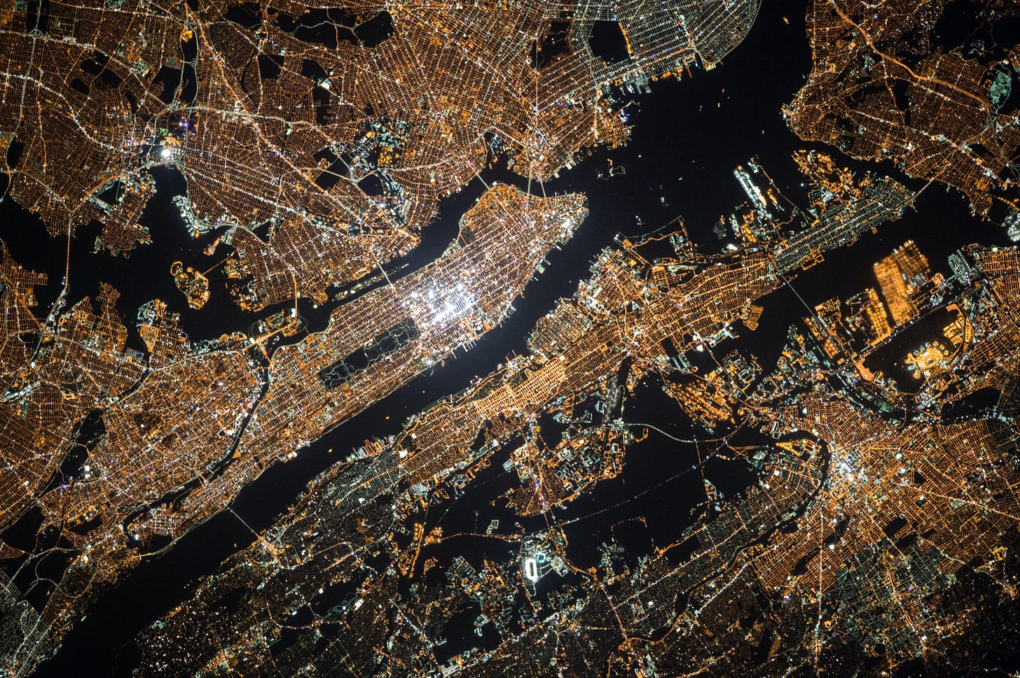 An aerial view of Manhattan at night, the city lights bright and crowded against the darkness of the rivers.