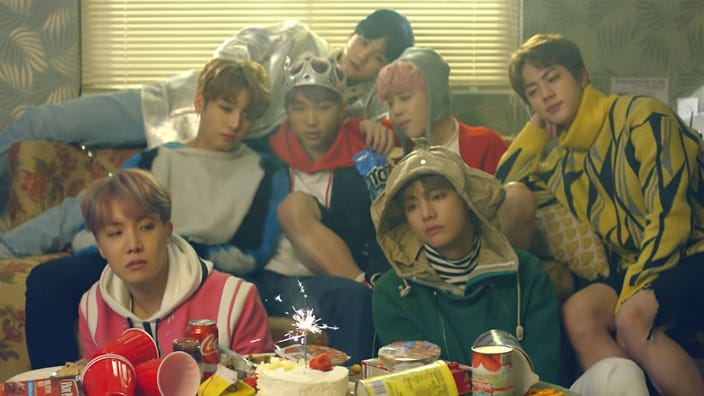 The members of BTS in their MV “Spring Day” staring at a fizzling birthday cake in a motel room.