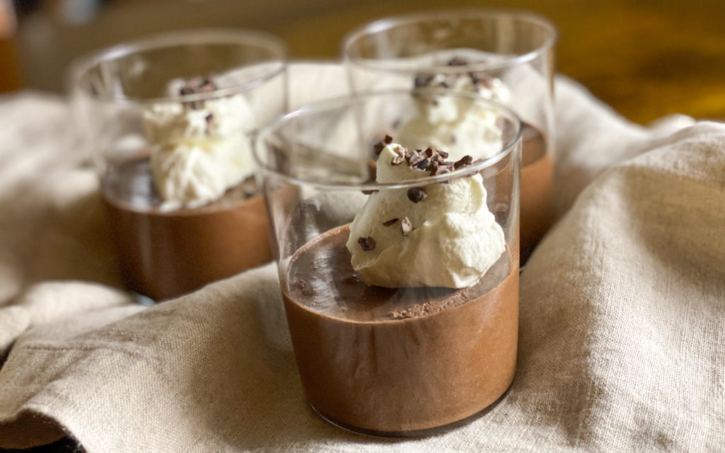 Three glasses of chocolate mousse topped with whipped cream and cacao nibs