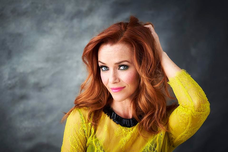 This image shows a studio portrait of Annie Wersching, who played the Borg Queen during Season 2 of Star Trek: Picard. Wersching, who passed away on 29 January 2023 at the age of 45, wears a yellow, see-through covering over a black dress.