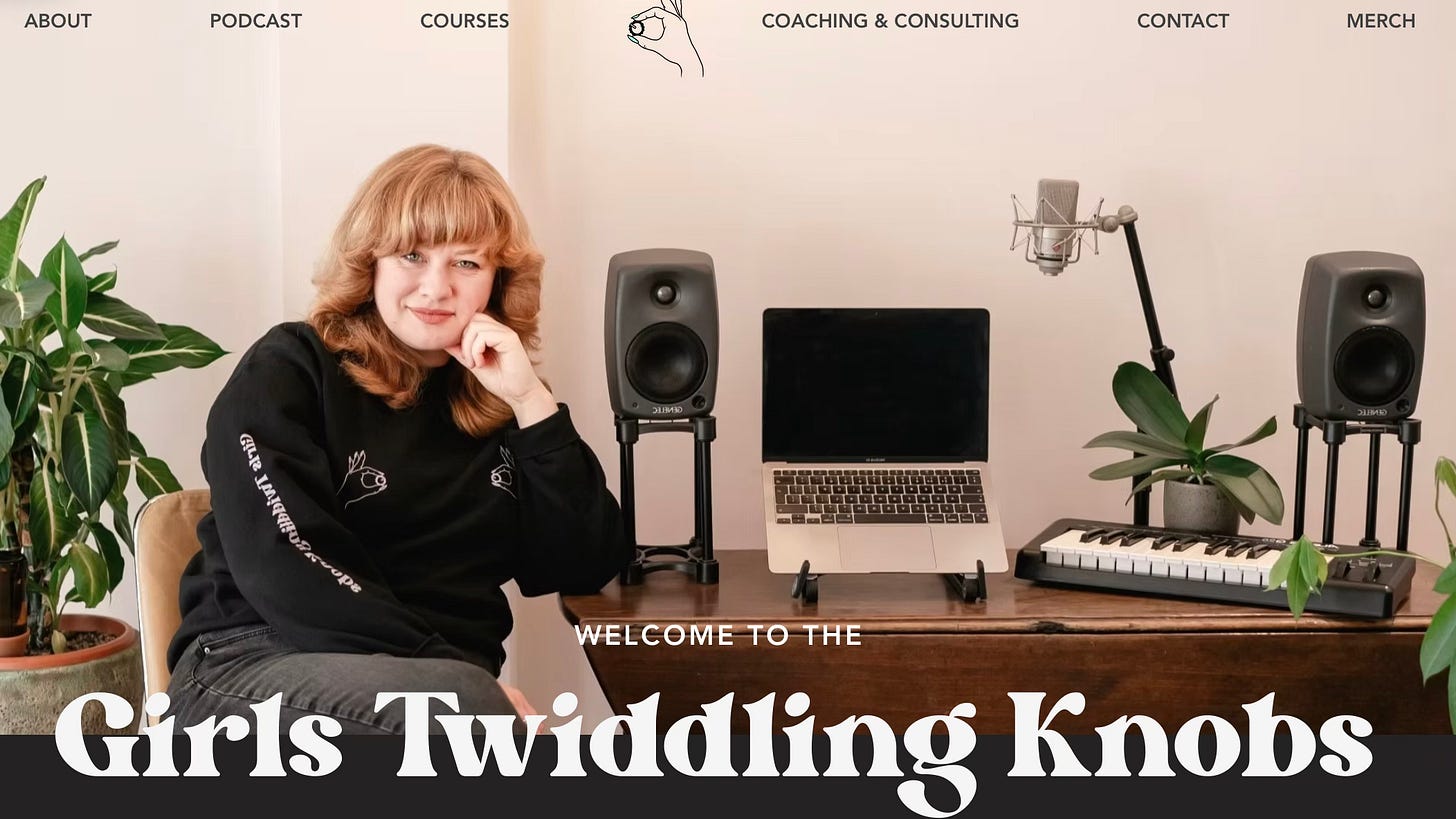 screen shot of the home page of Girls Twiddling Knobs, with the title in white text along the bottom and an image of Isobel Anderson, a white woman, with her elbow resting on a desk wearing a black top, the desk with an open laptop, keyboard and speakers.