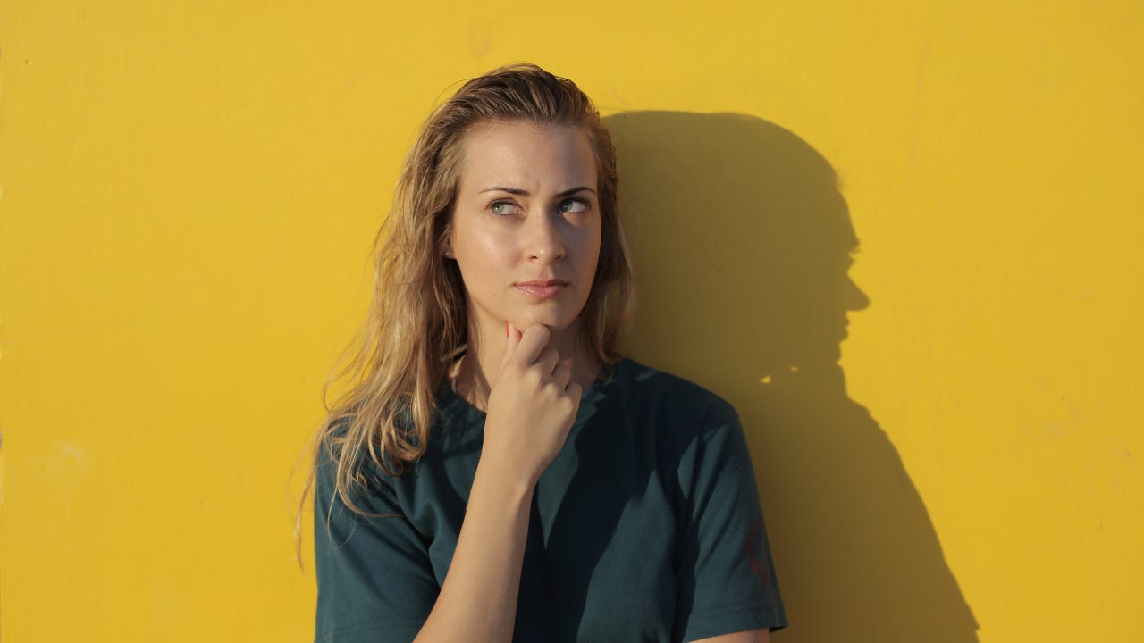 A woman thinking in front of a yellow background.
