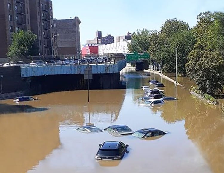 Color photo showing about a dozen abandoned, flooded cars in muddy brown water near an expressway exit in Brooklyn