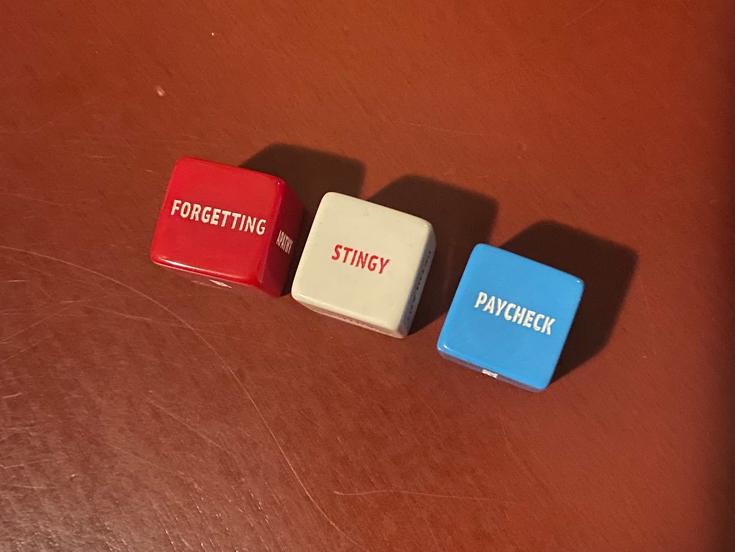 Red dice that says FORGETTING, a white dice that says "STINGY," and a blue dice that says "PAYCHECK"