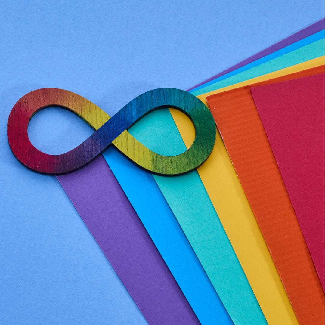 Image of a wooden cutout of a rainbow infinity on a blue background; under it are different stacks of various colored cardboard.