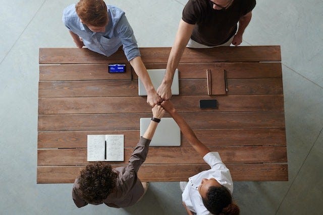 four people stand around a table and unite their fists in a show of teamwork