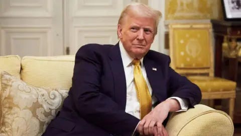 Getty Images Donald Trump, an elderly man with blonde hair, sits on a golden couch. He is wearing a blue suit with a white shirt and gold tie