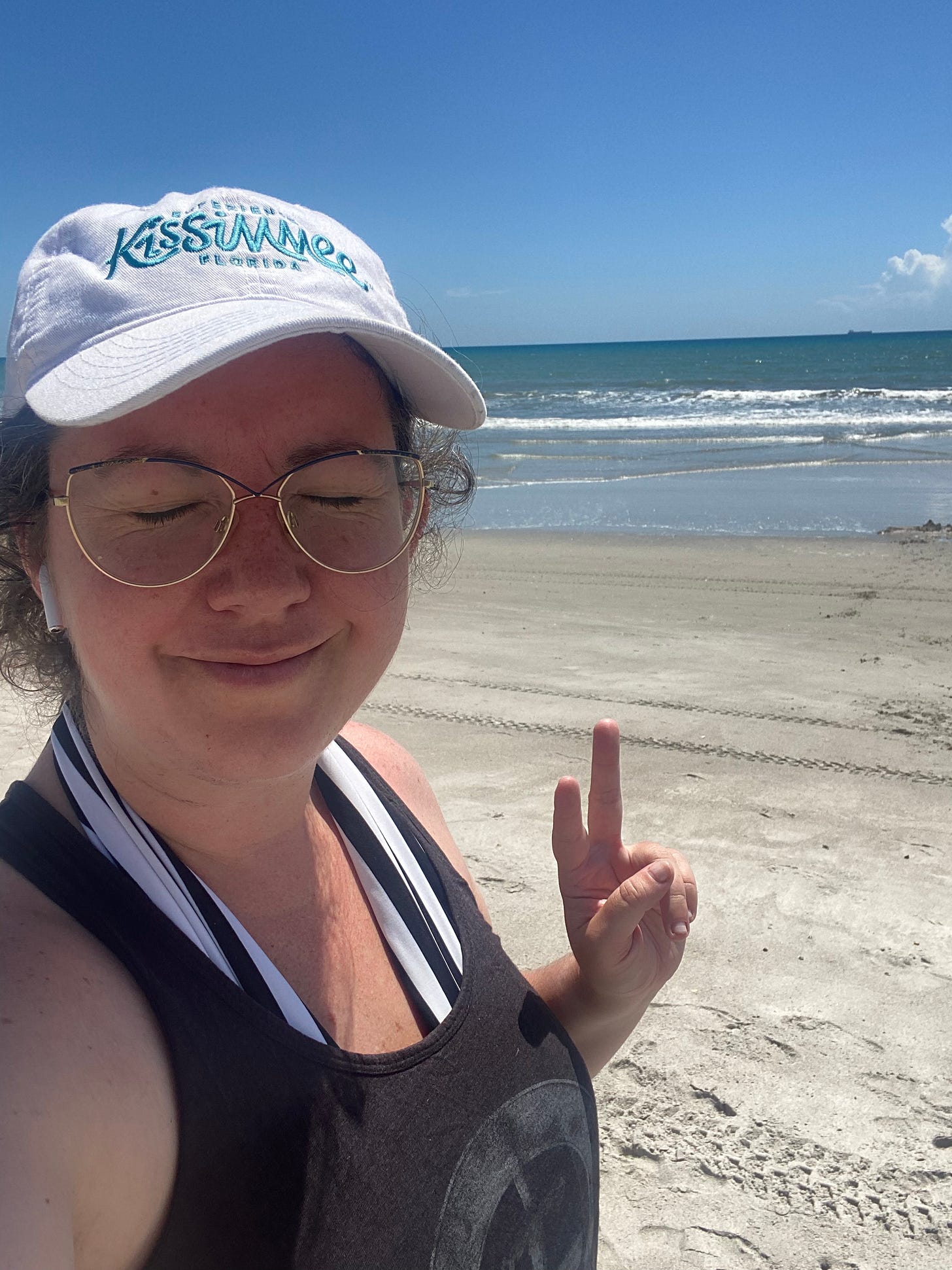 Meghan on a beach with her eyes closed and a Kissimmee hat.