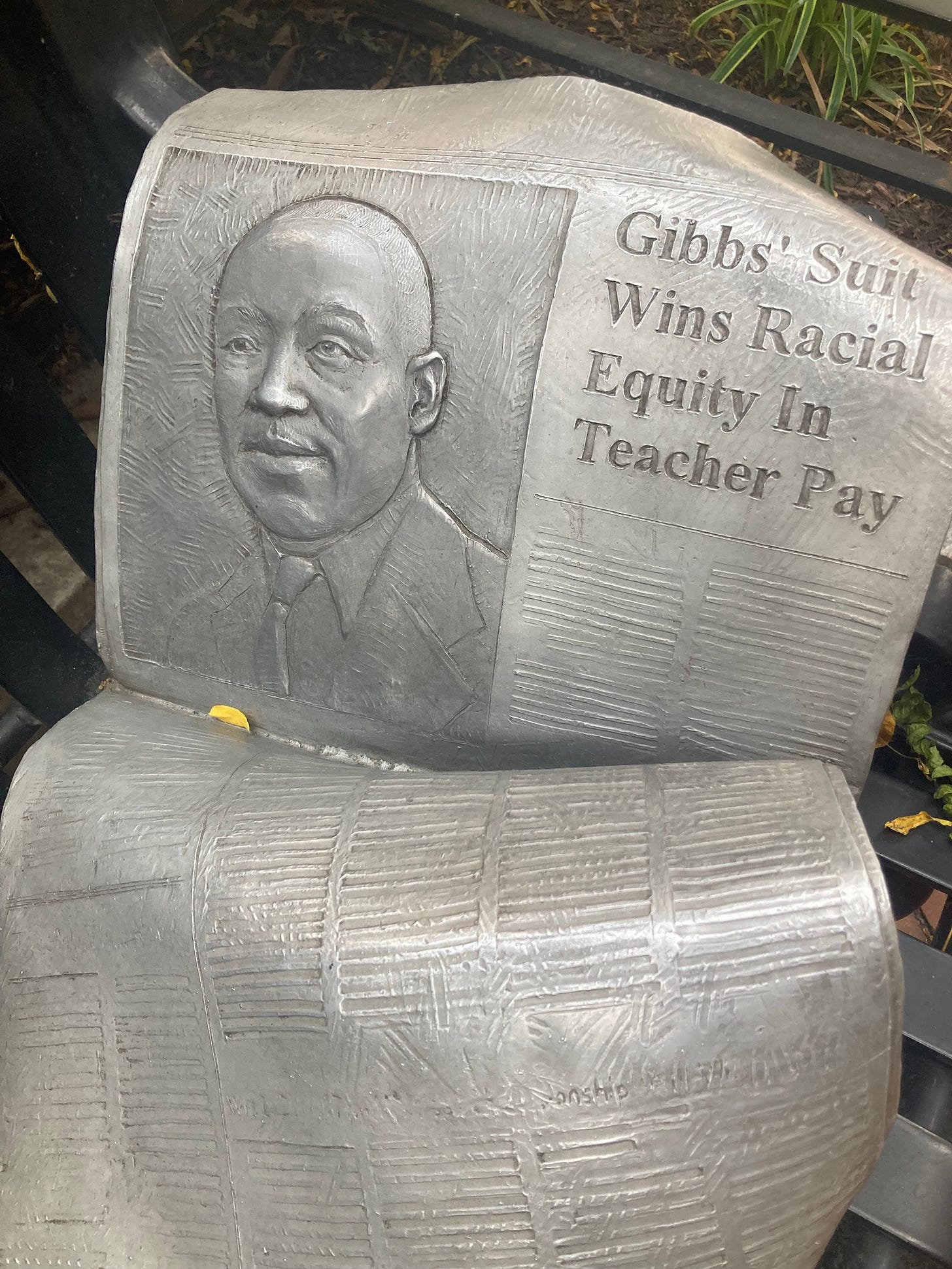 Statue of a newspaper with an engraving of Gibbs and the headline "Gibbs' Suit Wins Racial Equity in Teacher Pay"