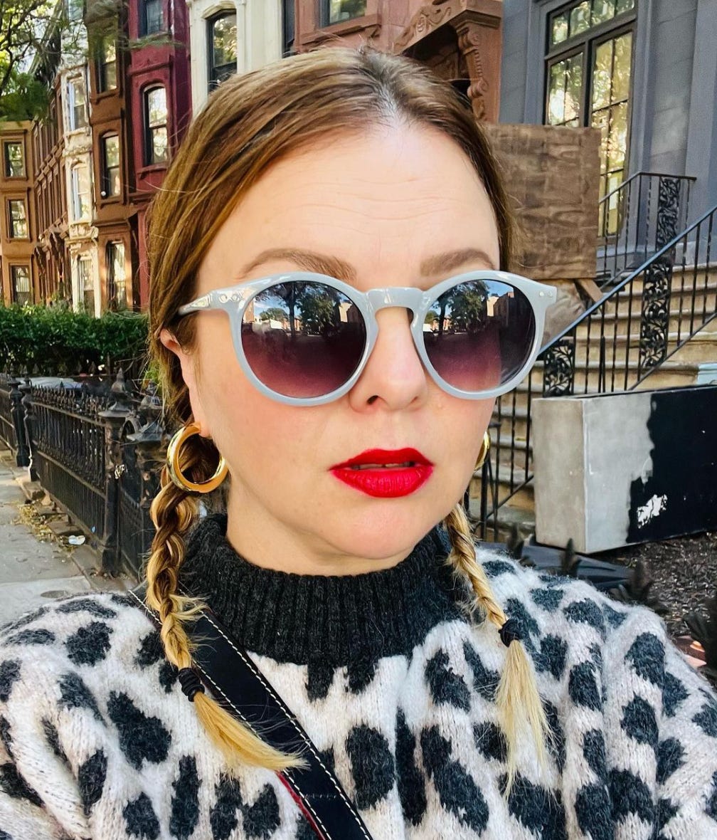 Amber walks down the street in New York. She wears sunglasses and a bright red lip.