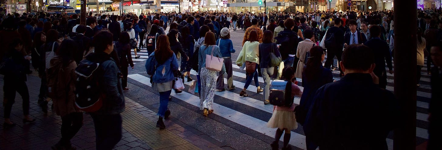 A large crowd of people cross a sidewalk in Tokyo.