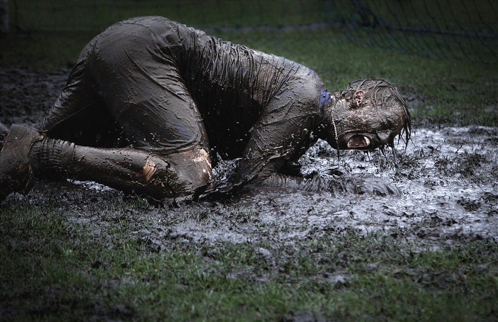 man lying on green grass soaked with mud