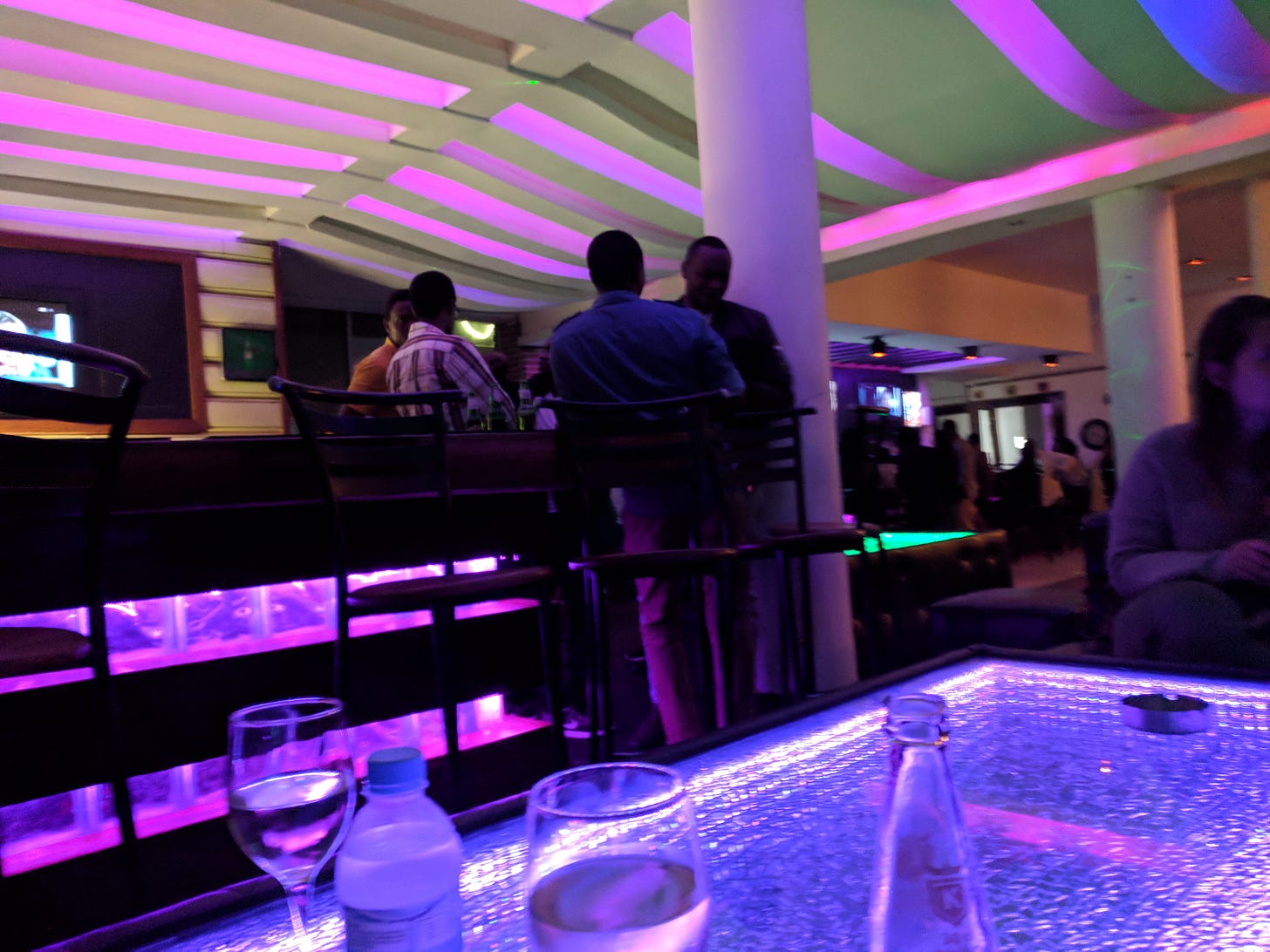 Inside a bar with drinks on a table. The bar is upscale, with purple lights emanating from the ceiling, bar and tabletop.