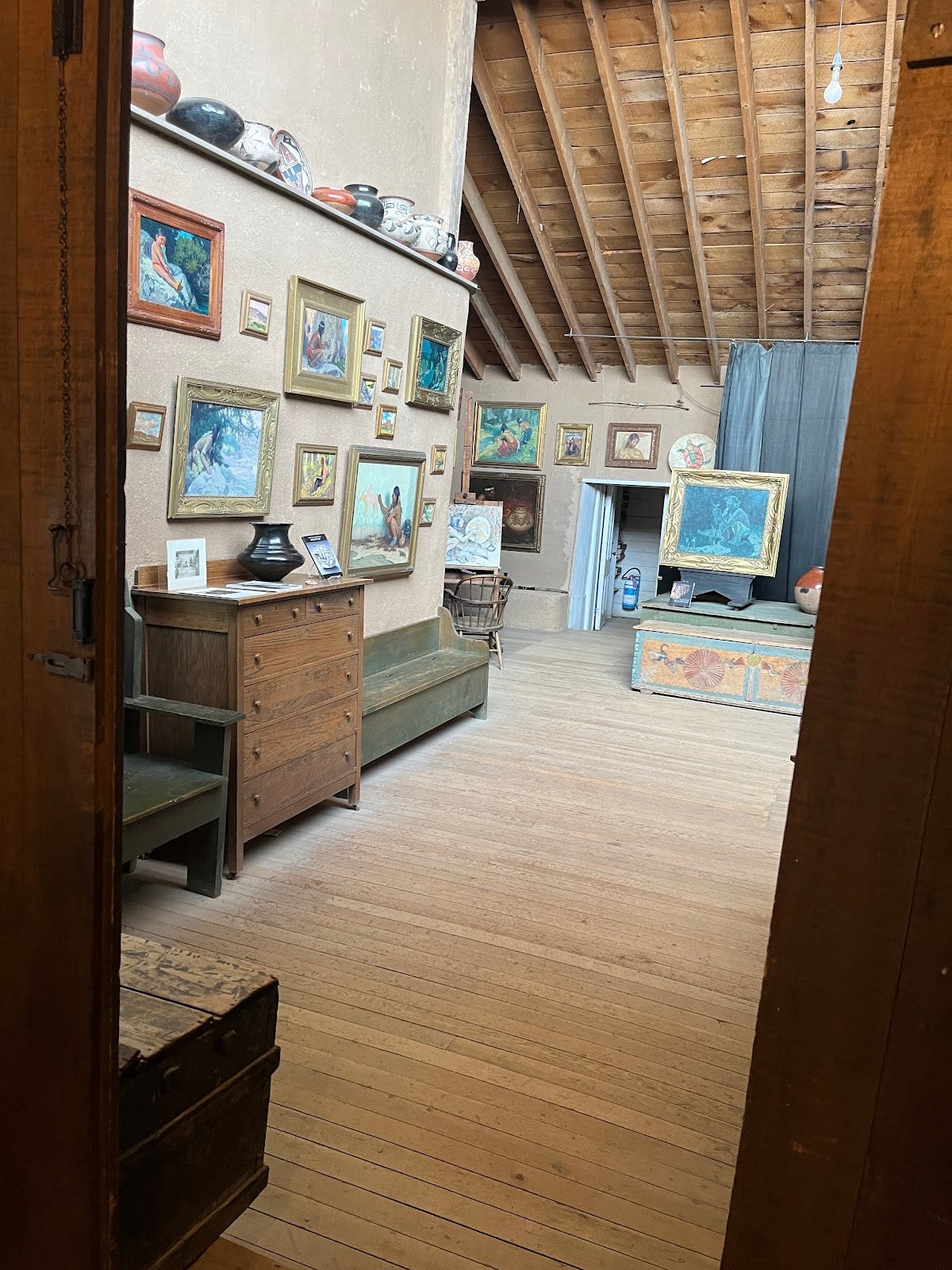 A photograph of E. Irving Couse's painting studio in Taos, New Mexico filled with framed pieces and pottery and a posing stage.