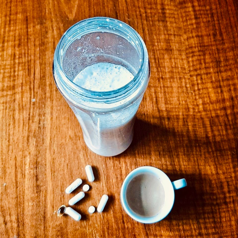 A smoothie, pills, and a coffee cup on a wooden surface