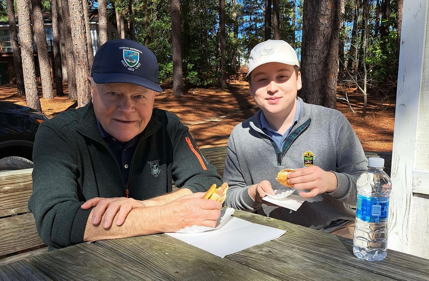 Dave Warren and Jake Patterson enjoy their hot dogs at a picnic table outside of the Mid Pines Golf Club's Halfway House.
