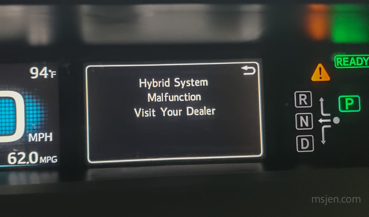 Car dashboard screen with a large warning text that says "Hybrid System Malfunction Visit Your Dealer", plus a yellow triangle with a ! in it.