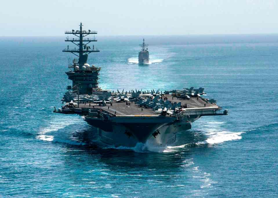 Aircraft carrier at sea, followed by two destroyers.