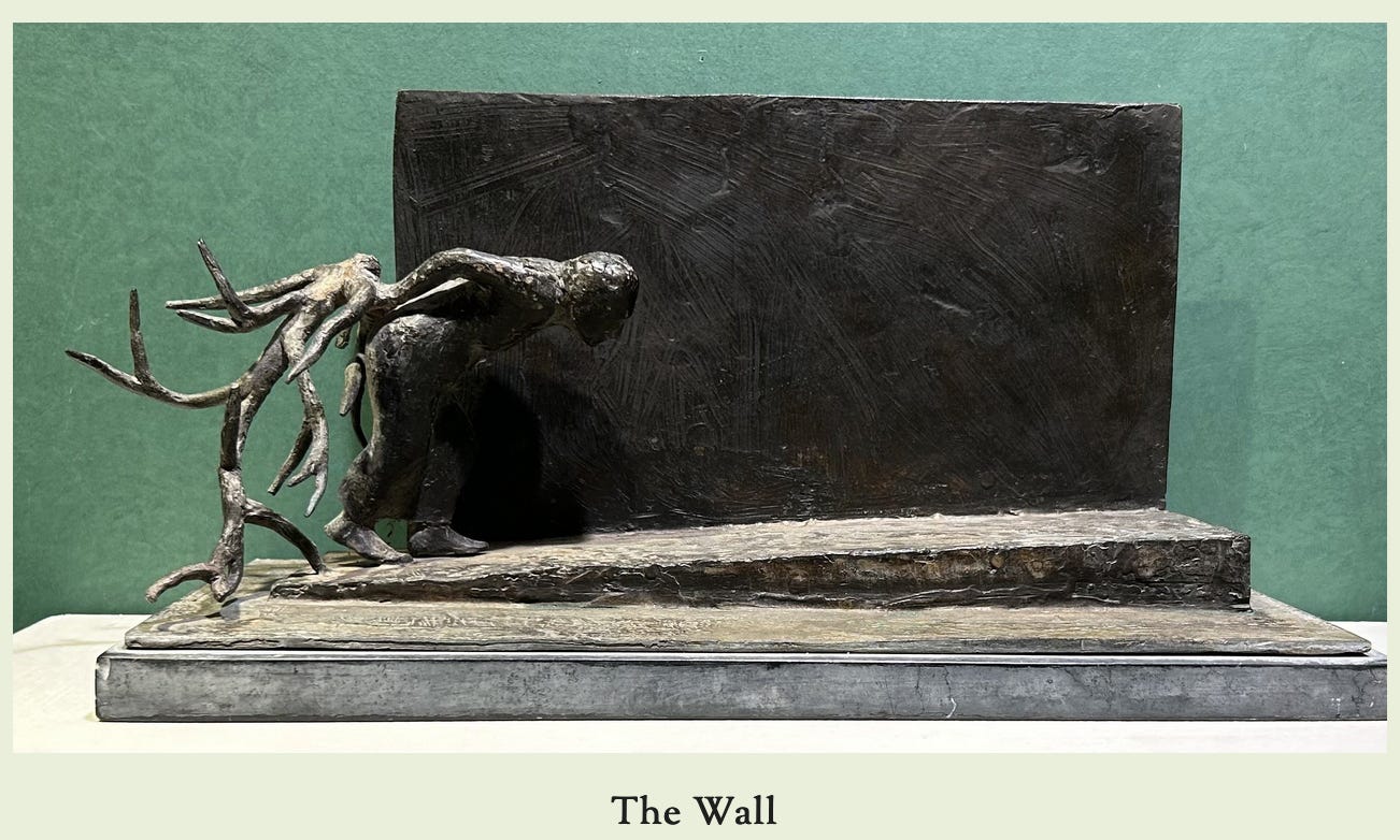 A sculpture by Syd Ginsberg called "The Wall" showing a figure of a person carrying a large branch on their back, walking up a gradual slope, with a wall behind them.