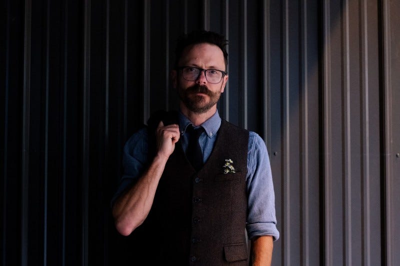 Kyle Joe wears a dark suit and stands in front of a gray background.