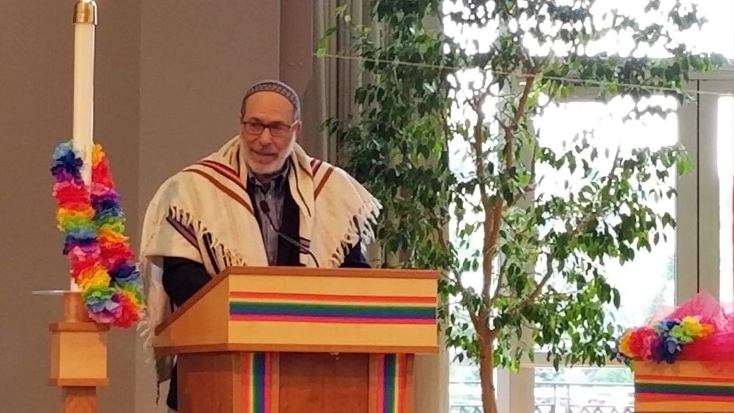 rabbi at podium with rainbow colored leis