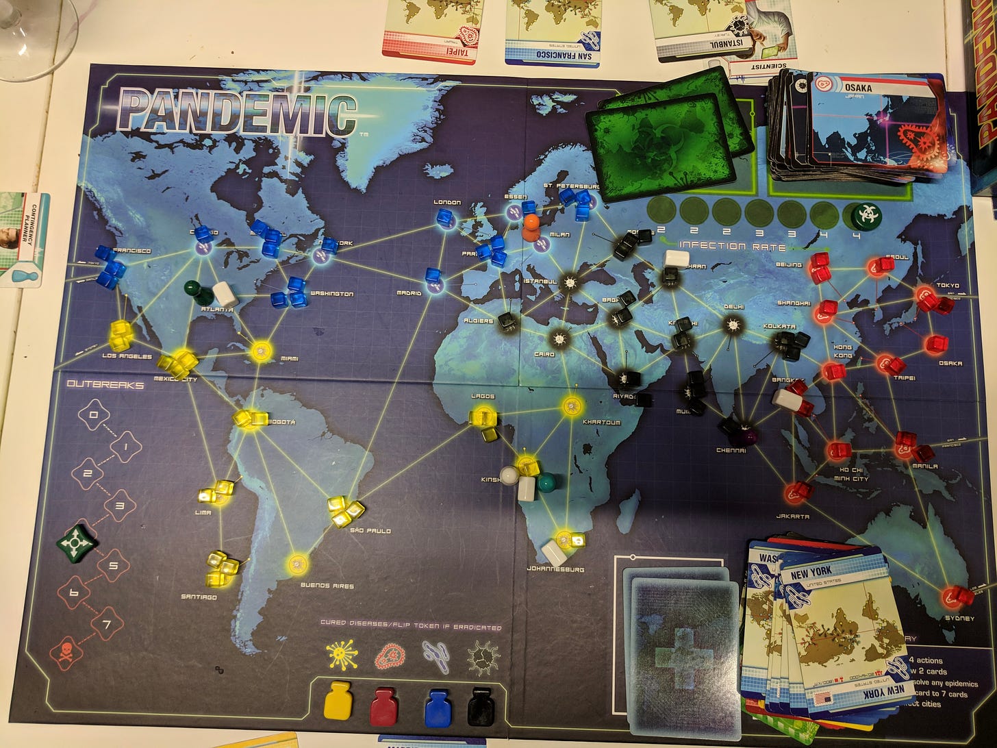 The board of the 'Pandemic' game. It is a map of the world with different cities noted with circles, and lines joining them. Coloured cubes representing diseases are placed all over the map.