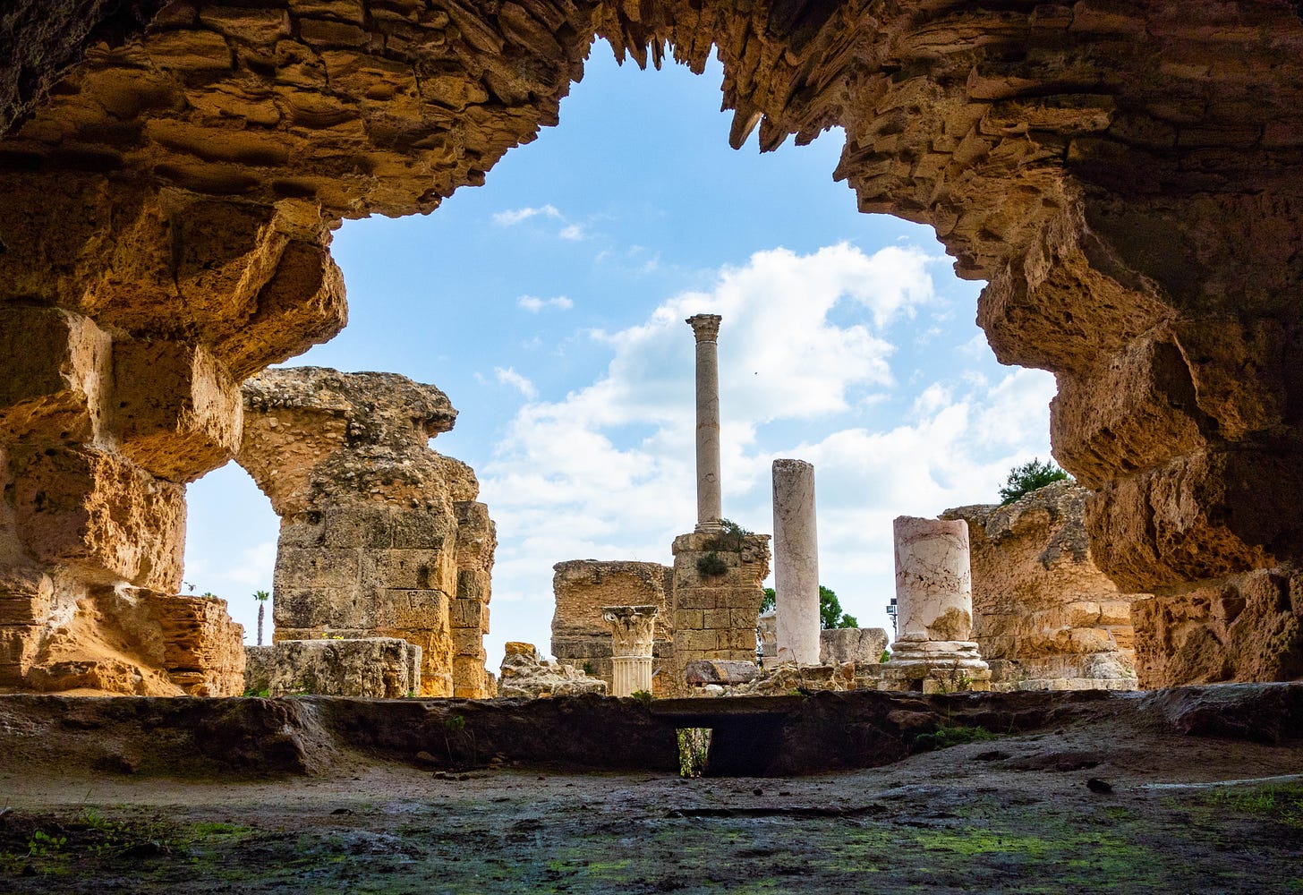 resti in pietra dorata e colonne di marmo della città di Cartagine inquadrati attraverso un'arcata di pietra