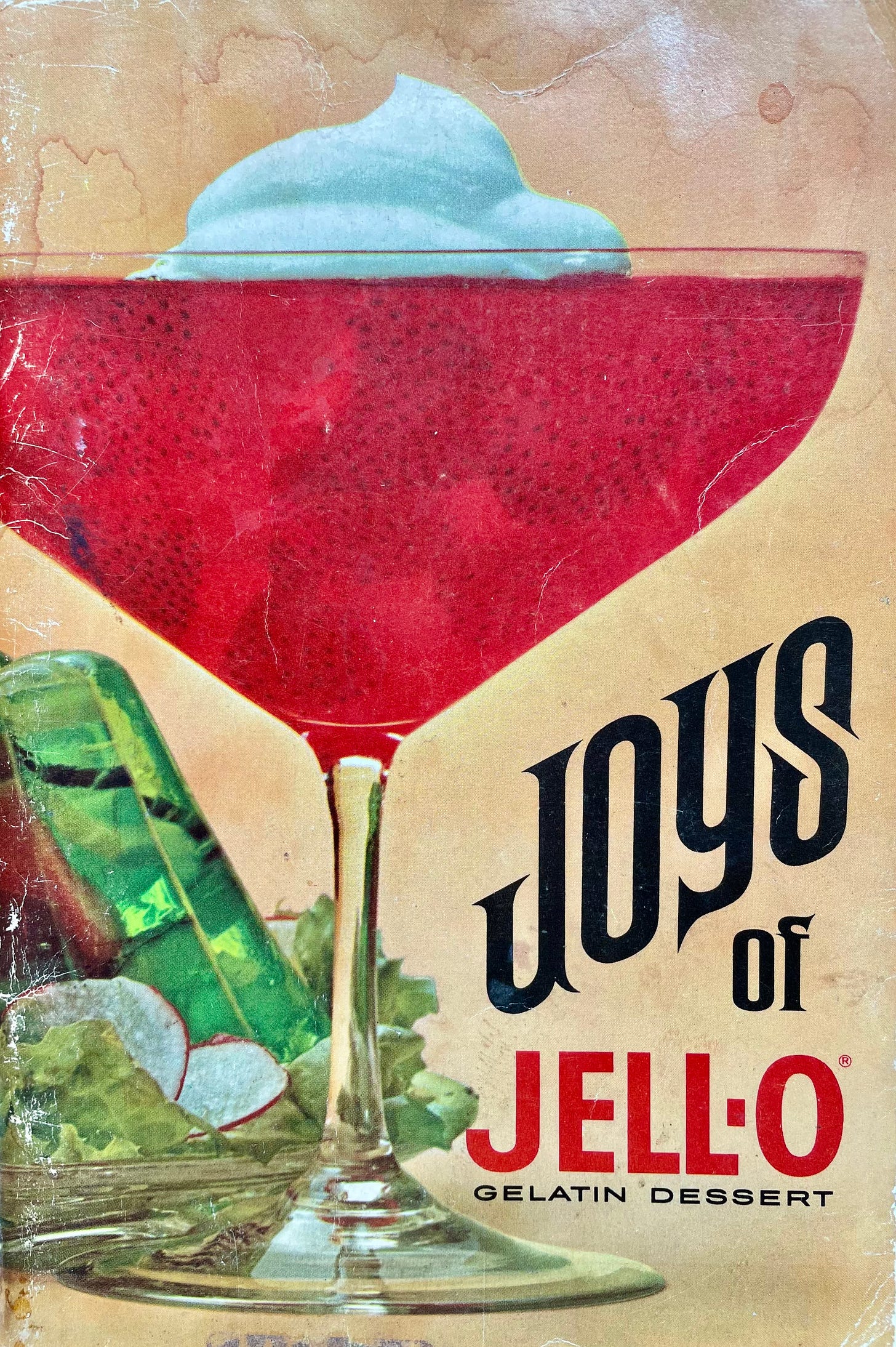 a copy of the 1968 Joys of Jello with a strawberry jello parfait in a stemmed glass