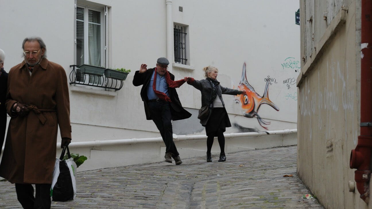 A still from the movie Le Week-end. An older couple dances on a cobblestone street.