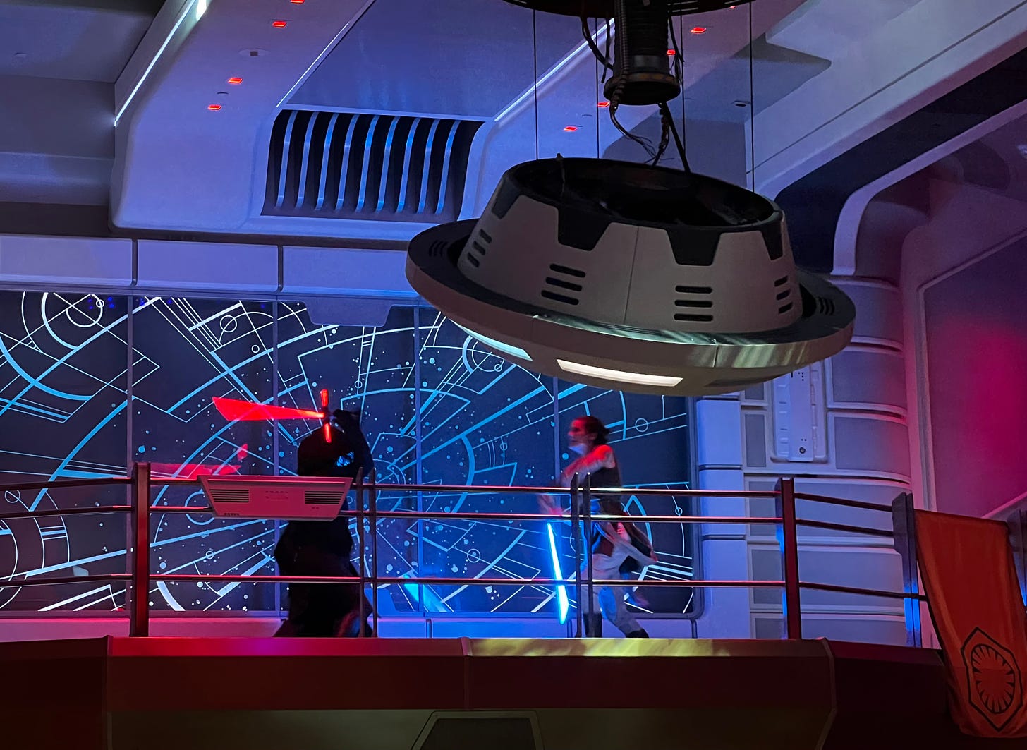 Rey and Kylo Ren fighting with lightsabers. A big lighting fixture is detached from the ceiling.