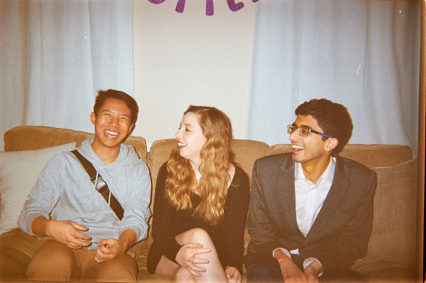 Charles, Eliza, and Ashwin (left-to-right) seated laughing on a couch. Vintage style photo